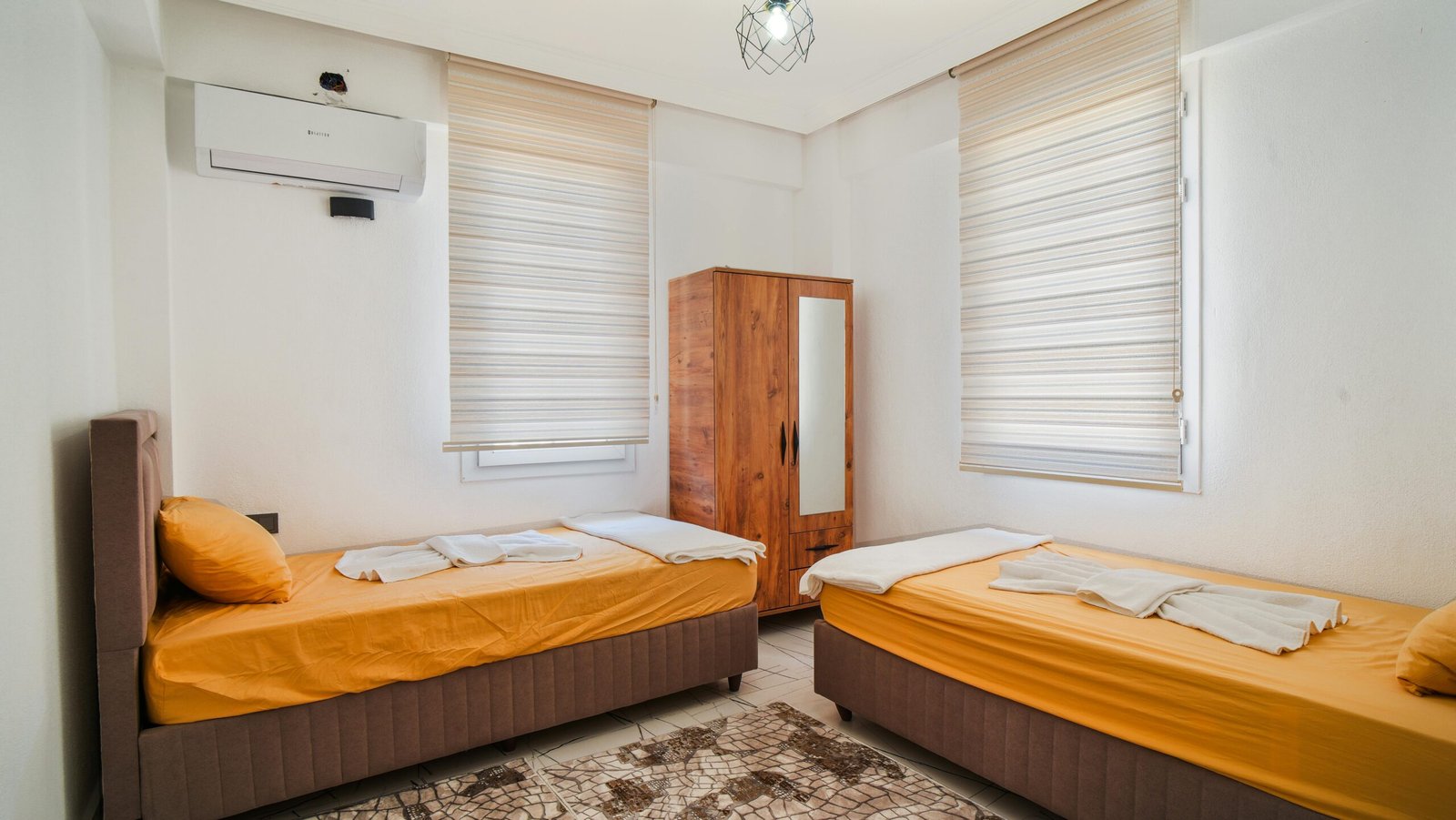 A bright, modern bedroom featuring two twin beds with orange linens, perfect for guests.